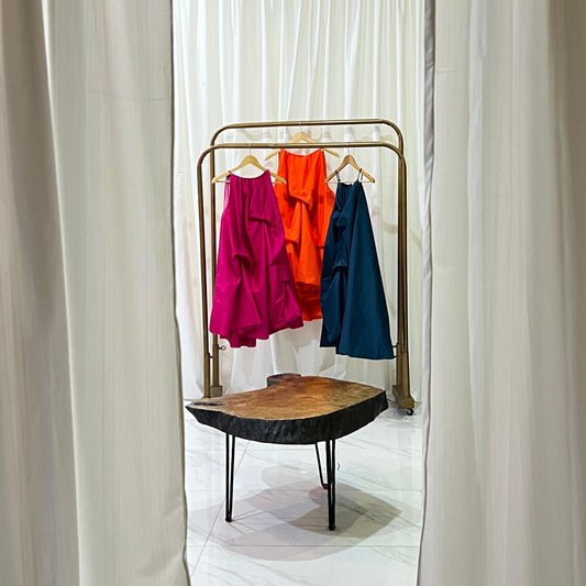 Three colorful dresses hanging on a rack with white curtains on either side.