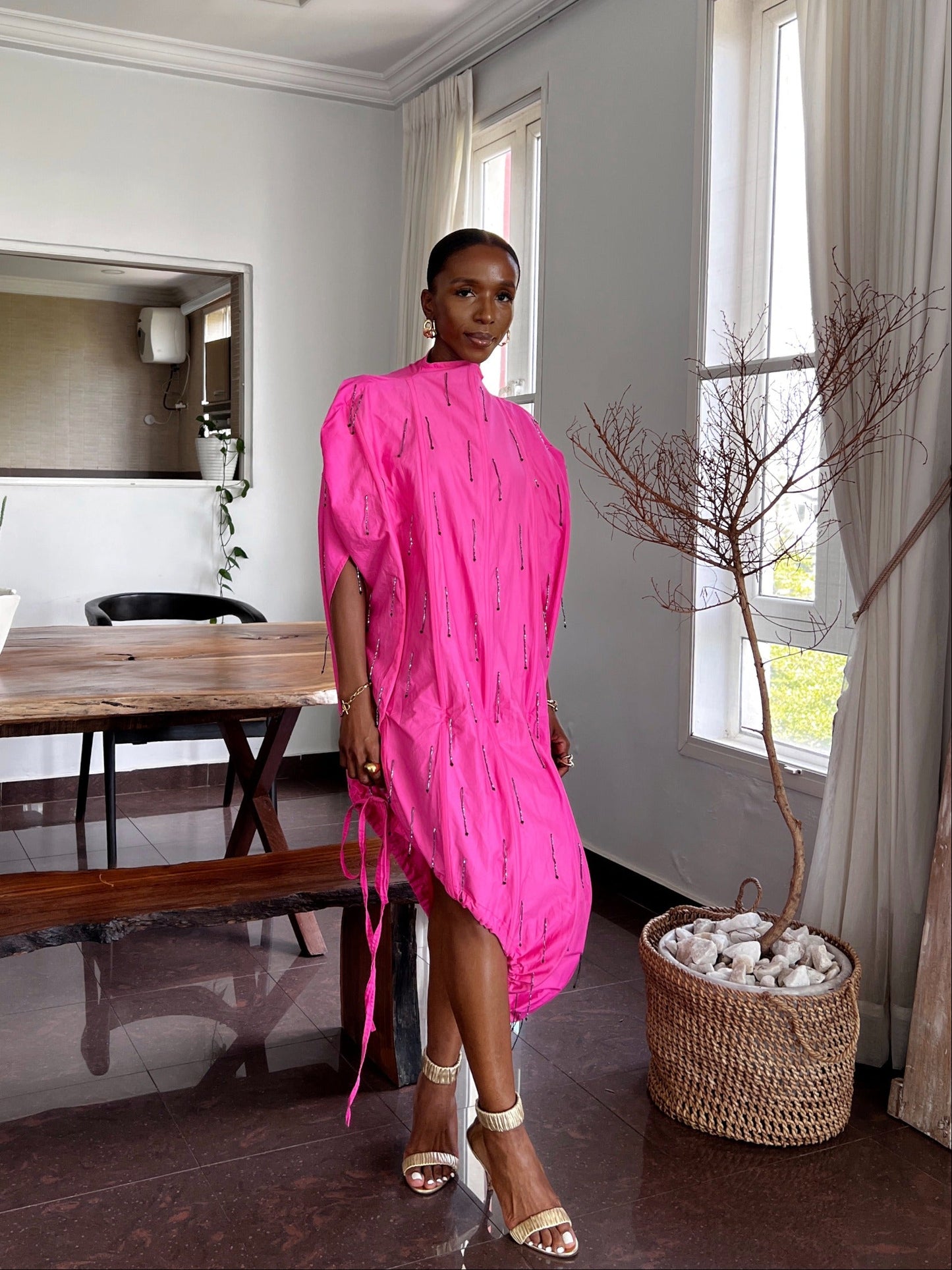 Woman in a bright pink dress standing in a modern living room.